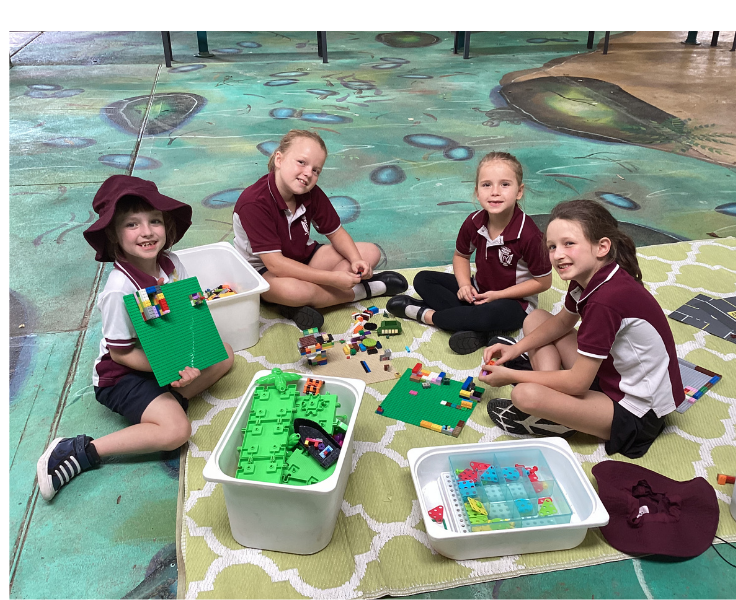 four girls sitting outside on mural covered covered play on mats with games