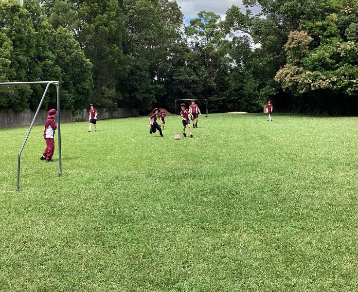 A group of students on a large green soccer field playing soccer.