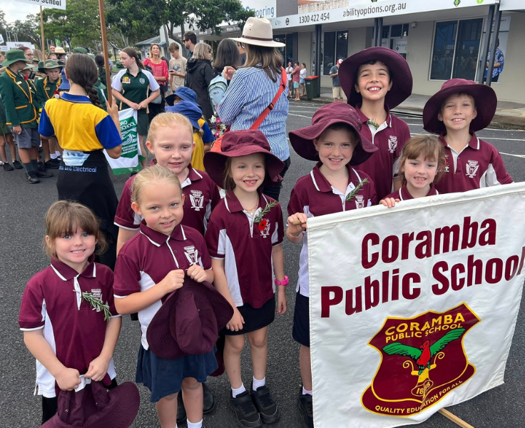 Eight students dressed in school uniform standing behind the school banner ready to participate in the ANZAC march.