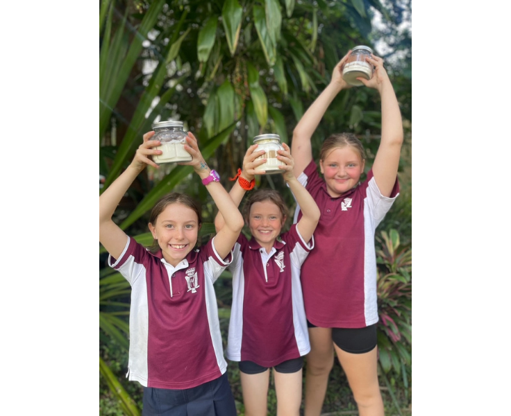 Three female students holding recipe jars above their head, a fundraising initiative