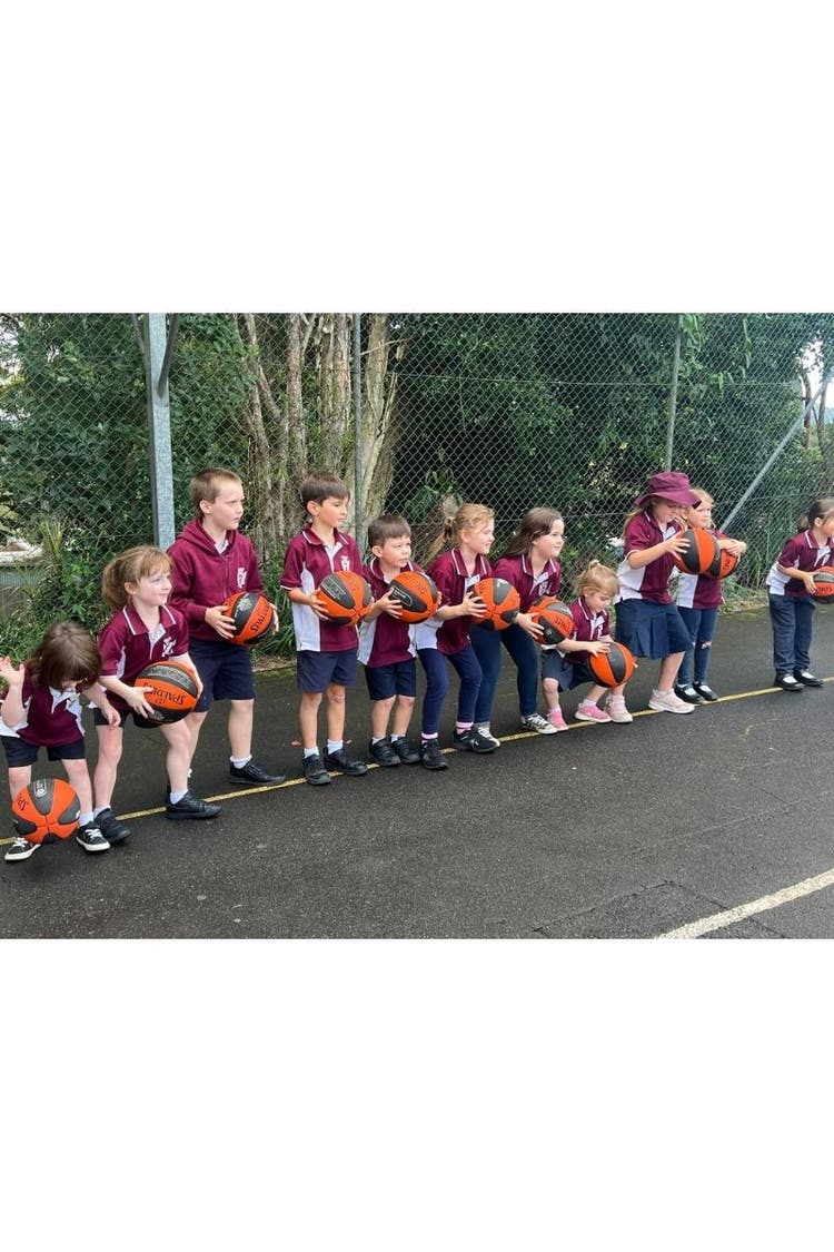A line of students with basketballs in their hands on the basketball courts waiting for instructions