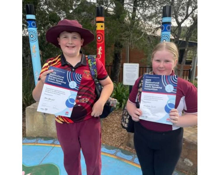 A year 6 boy and girl standing in front of totem poles with awards