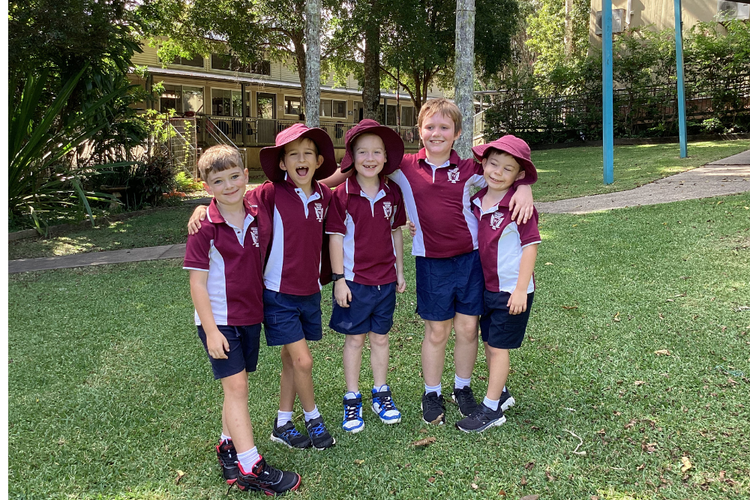 Five young boys in school uniform outside standing together in a line with arms around each others shoulders