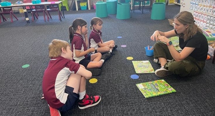 teacher sitting on the floor giving lesson to three young students