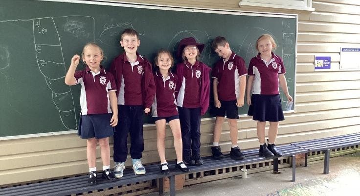 six students standing along the front of a big chalk board