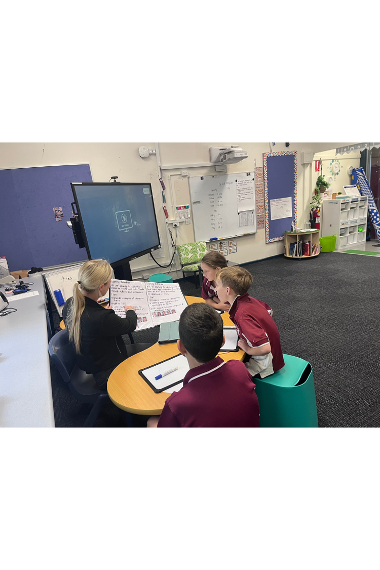 three students sitting around desk with principal doing small group learning