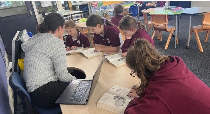 a teacher in 3-6 class at a desk with four students reading together