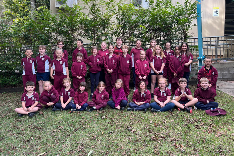 Whole school photo of all students in school uniform sitting and standing as a group outside.