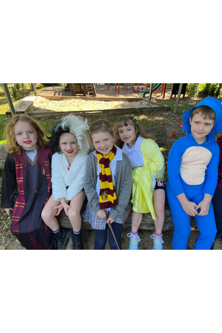 five students sitting on a bench dressed up as book characters looking at camera