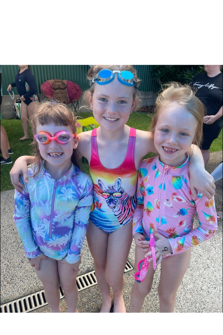 Three young girls in swimmers and googles on waiting for a race at the school swimming carnival.